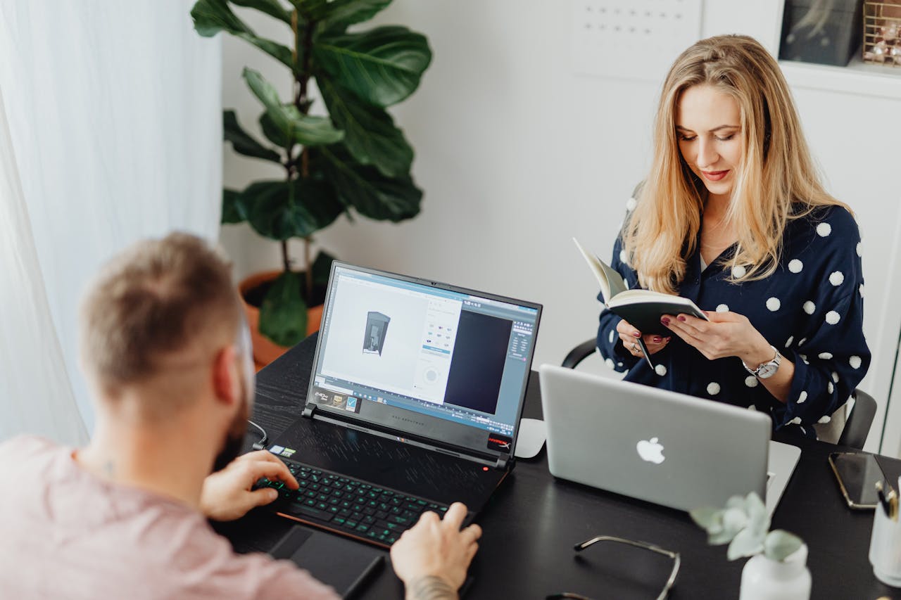 Professional coworkers collaborating in a modern office setting with laptops and a notebook.